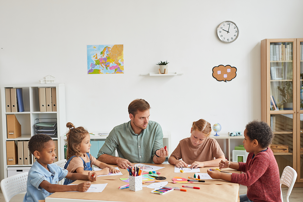 male-teacher-working-with-multi-ethnic-group-children-drawing-pictures-during-art-class-school-development-center
